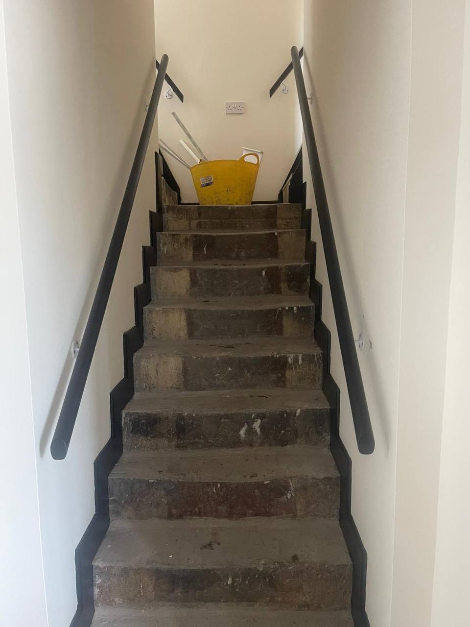 Narrow stairwell with freshly painted walls and dark grey handrails